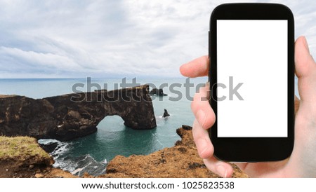 travel concept - tourist photographs stone arch on Dyrholaey cliff near Vik I Myrdal village in Iceland on Atlantic Coast in september on smartphone with cut out screen for advertising logo