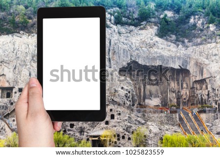 travel concept - tourist photographs West Hill with The Big Vairocana statue of Chinese Buddhist monument Longmen Caves (Dragon's Gate Grottoes) on tablet with cut out screen for advertising logo