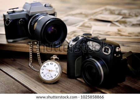 Close up antique pocket watch, vintage photographic prints, film camera and digital compact on aged wooden background.