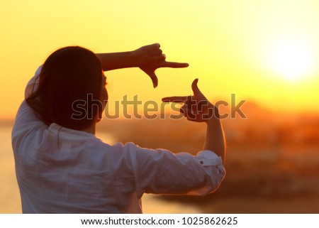 Back view backlight portrait of a woman framing with fingers at sunset