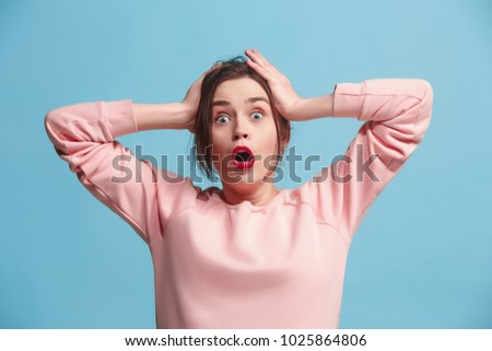 Beautiful female half-length portrait isolated on blue studio backgroud. The young emotional surprised woman holding hands by the head and looking at camera. The human emotions, facial expression Royalty-Free Stock Photo #1025864806