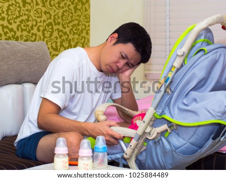 Father tired and asleep  his newborn baby boy with milk bottle sitting on a white couch in living room at home