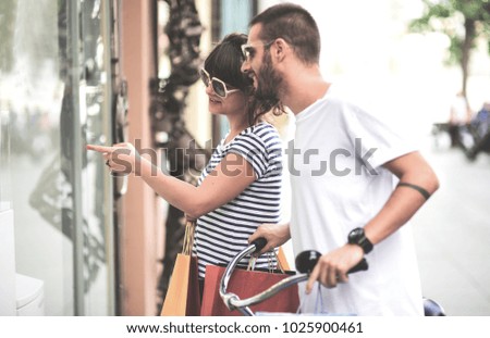 Beautiful happy couple pushing bicycle in the city and holding shopping bags. Urban Shopping concept.