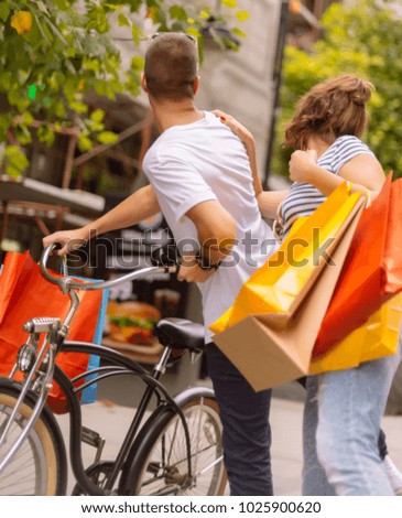 Beautiful happy couple pushing bicycle in the city and holding shopping bags. Urban Shopping concept.