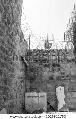 Vertical, black and white picture of brick wall with barbwire in Hebron, located in West bank, Israel.