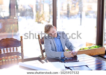 Hardworking student preparing before exam in fast motion at cafe with papers and typing by tablet in fast motion. Young guy wears smart watch and grey suit. Concept of preparing before exam using