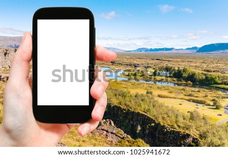 travel concept - tourist photographs rift valley with earth fault in Thingvellir national park in Iceland on smartphone with cut out screen for advertising logo