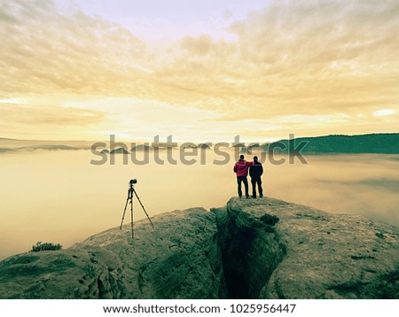 Two warm coat photographers with tripod shoot pictures of autumnal landscape below mountain.  Rainy misty day in  mountains with  cloudy sky, cold in the morning