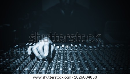 male sound engineer hands working on audio mixing console in recording studio