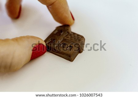 Close-up of a small candy in the shape of a chocolate house in the hand of a young woman on a white background, shallow depth of focus. Concept sweet home.