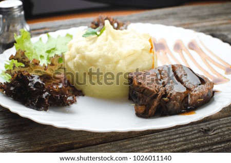 On a white plate, on a wooden background, mashed potatoes with beef meat beautifully polished balsamic sauce