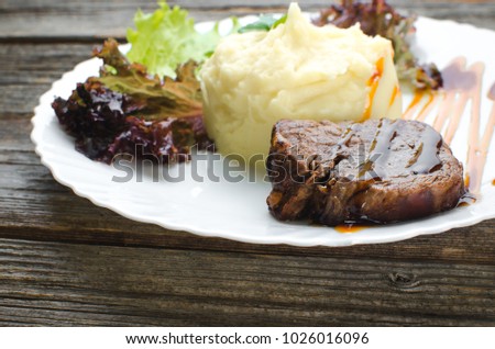On a white plate, on a wooden background, mashed potatoes with beef meat beautifully polished balsamic sauce