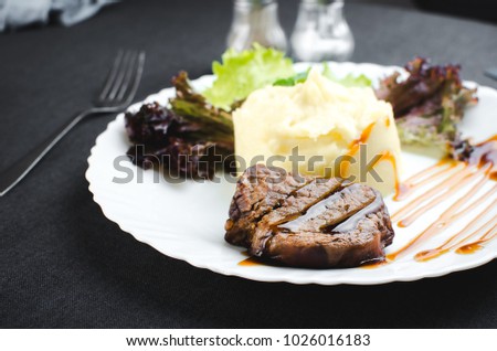 On a white plate, on a beautiful fabric and dark background mashed potatoes with beef meat beautifully polished balsamic sauce