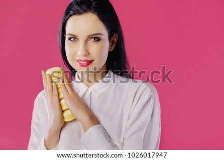 Picture of cheerful girl in white blouse holding piece of cake. Girl on a pink background