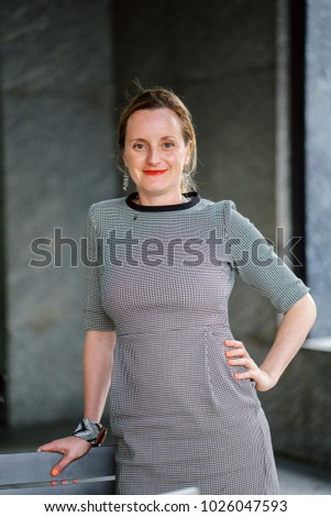 Portrait of a professional, neat and well put-together Caucasian woman in her office of glass and marble. She is smiling and relaxed, confident and cheerful.