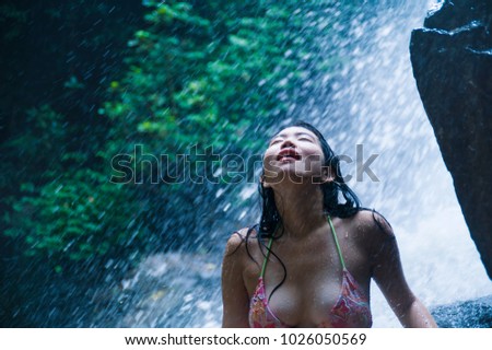 portrait of young beautiful Asian woman looking pure and enjoying nature beauty with face wet under amazing beautiful natural waterfall in tropical paradise in tourist destination and adventure travel