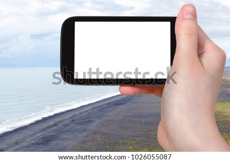 travel concept - tourist photographs Solheimafjara black sand beach from Dyrholaey promontory on Atlantic Coast in Iceland in september on smartphone with cut out screen for advertising logo