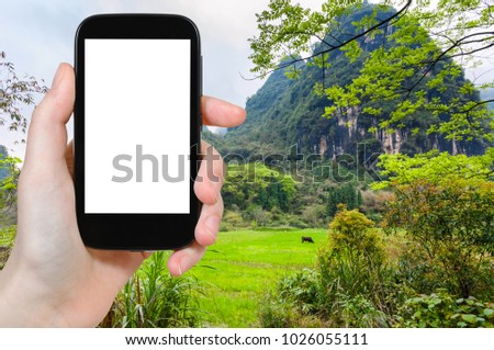 travel concept - tourist photographs green meadow near karst mountain in Yangshuo County in China in spring season on smartphone with cut out screen for advertising logo