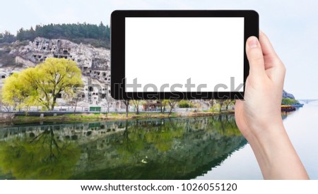 travel concept - tourist photographs Yi River and West Hill with Chinese Buddhist monument Longmen Grottoes (Dragon's Gate) in China on tablet with cut out screen for advertising logo in spring