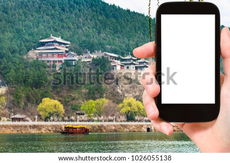 travel concept - tourist photographs temples on East Hill of Chinese Buddhist monument Longmen Caves (Dragon's Gate Grottoes) through Yi river on smartphone with cut out screen for advertising logo