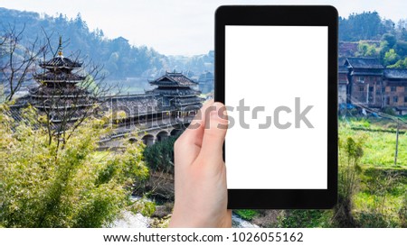 travel concept - tourist photographs Wind and Rain (Fengyu) bridge in Chengyang village of Sanjiang Dong Autonomous County in China in spring on tablet with cut out screen for advertising