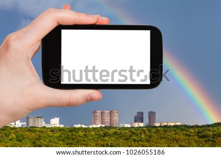 travel concept - tourist photographs rainbow over modern urban houses and green park in Moscow city in Russia in summer on smartphone with cut out screen for advertising logo