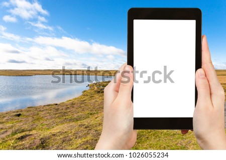 travel concept - tourist photographs tundra landscape near Leirvogsvatn lake in Iceland in autumn on tablet with cut out screen for advertising logo