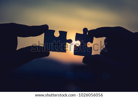Two hands trying to connect couple puzzle piece with sunset background. Jigsaw alone wooden puzzle against sun rays. one part of whole. symbol of association and connection. business strategy.
