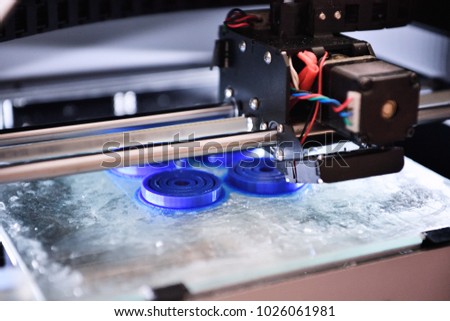 The 3D printer prints the details of the blue plastic. 3D printing of ABS or PLA plastic on a transparent glass platform.