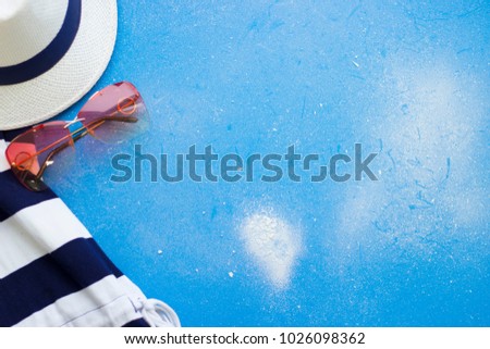 Blue travelling background with summer ansemble of a straw hat, shirt and sunglasses. Travel concept. Space for text or product display.