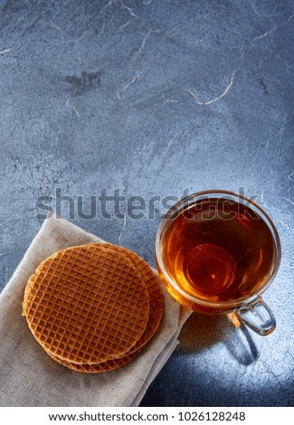 Vertical picture of a glass cup of black tea with waffles on a dark greyish marble background. Top view