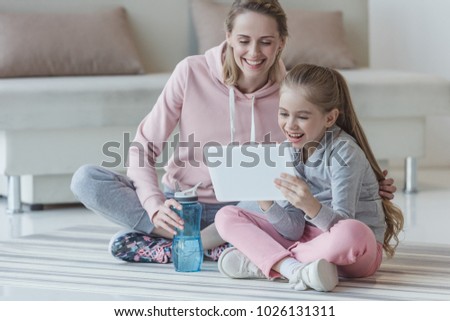 mother and daughter using tablet while sitting on yoga mat