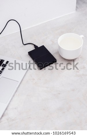 External hard drive connected to the laptop and white mug on grey concrete background. File storage, back up, info recovery concept. Flat lay, copyspace for text.