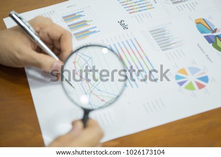 Hand of businessman holding a glass  and   text on chart on the desk, finance and business concept.