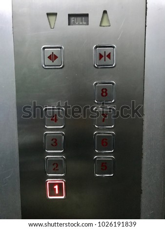 An old elevator has some scratches on surfaces. The material of construction are cement, aluminum and plastic. The lift which has buttons of each floor is vintage or retro style.