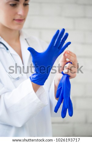 Portrait of the young brunette nurse who is taking off the blue gloves indoors