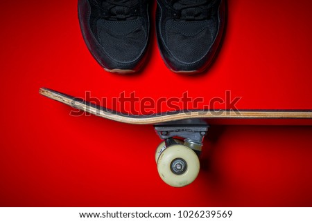 Black men's shoes and used skateboard on a red background
