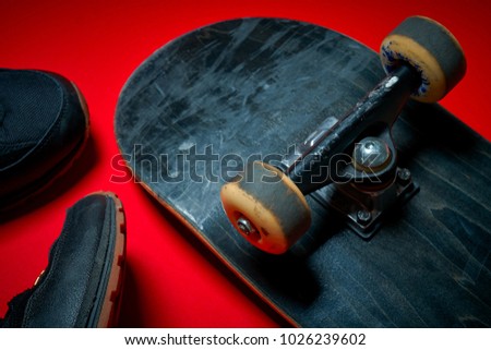 Black men's shoes and used skateboard on a red background