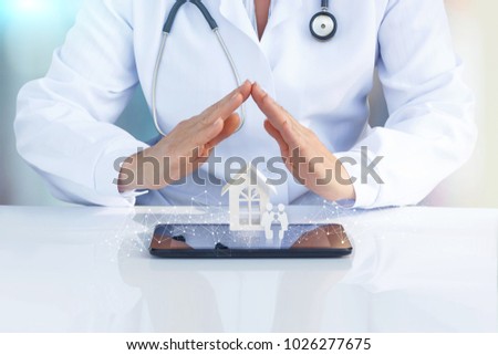 Doctor at the table with his hands to protect the icon the family and home. The concept of health insurance of the family.