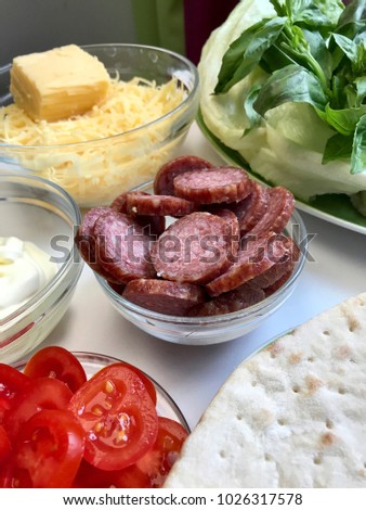 Preparation of pizza. Necessary ingredients are on the table: cheese, sausage, pizza base and vegetables.