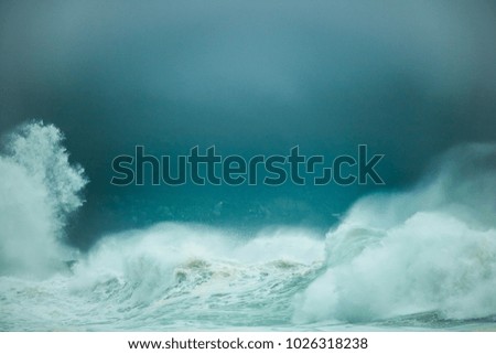 Huge waves crashing on a beach on a misty dark day with mountain in the background.