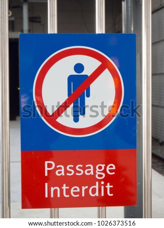 Forbidden area sign, in french, displaying a man icon and words "passage interdit", mounted on metallic vertical bars