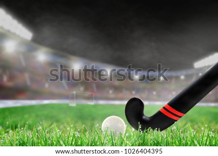 Field hockey stick and ball on grass in brightly lit outdoor stadium with focus on foreground and shallow depth of field on background. Deliberate lens flare and copy space.