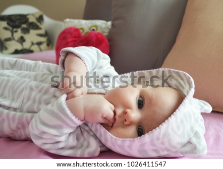 Cute infant baby 3 months old in Hooded Fleece Jumpsuit eating hand