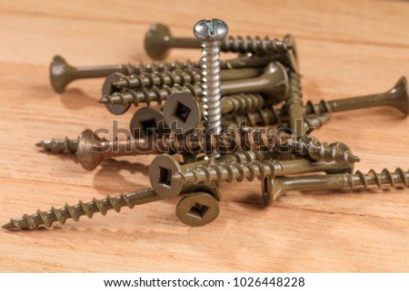 Used screws for construction projects on a wooden board background. Screw that is installed up in place, along with other screws in the lying position. Renovation and constructon conceptual picture.
