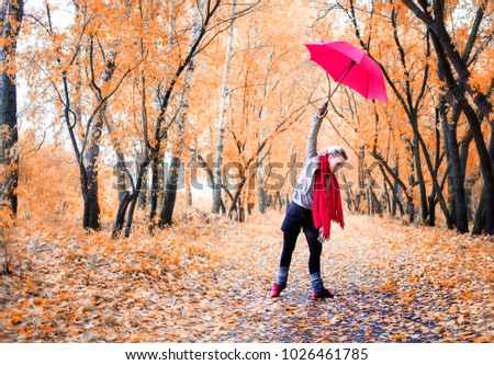 blonde girl in red scarf and with red umbrella dancing in yellow autumn forest 