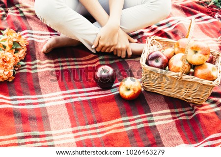 Autumn picnic concept scene with blanket, apples, flowers and a young lady partially pictured.