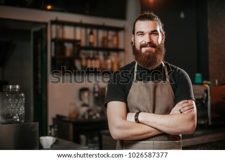 Portrait of bearded happy barista standing at trendy coffee shop, cafe - small business concept. Hipster barista man with beard. Royalty-Free Stock Photo #1026587377