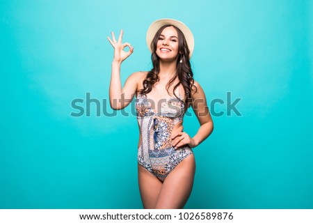 Positive beautiful young woman in bikini showing ok gesture isolated over green