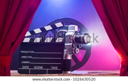 Illuminated Movie Camera With Clapperboard And Film Reel Against Colored Background